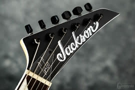 Na główce o charakterystycznym dla gitary marki Jackson kształcie umieszczono 6 firmowych kluczy, logo producenta oraz płytkę maskującą z autografem Gusa G.